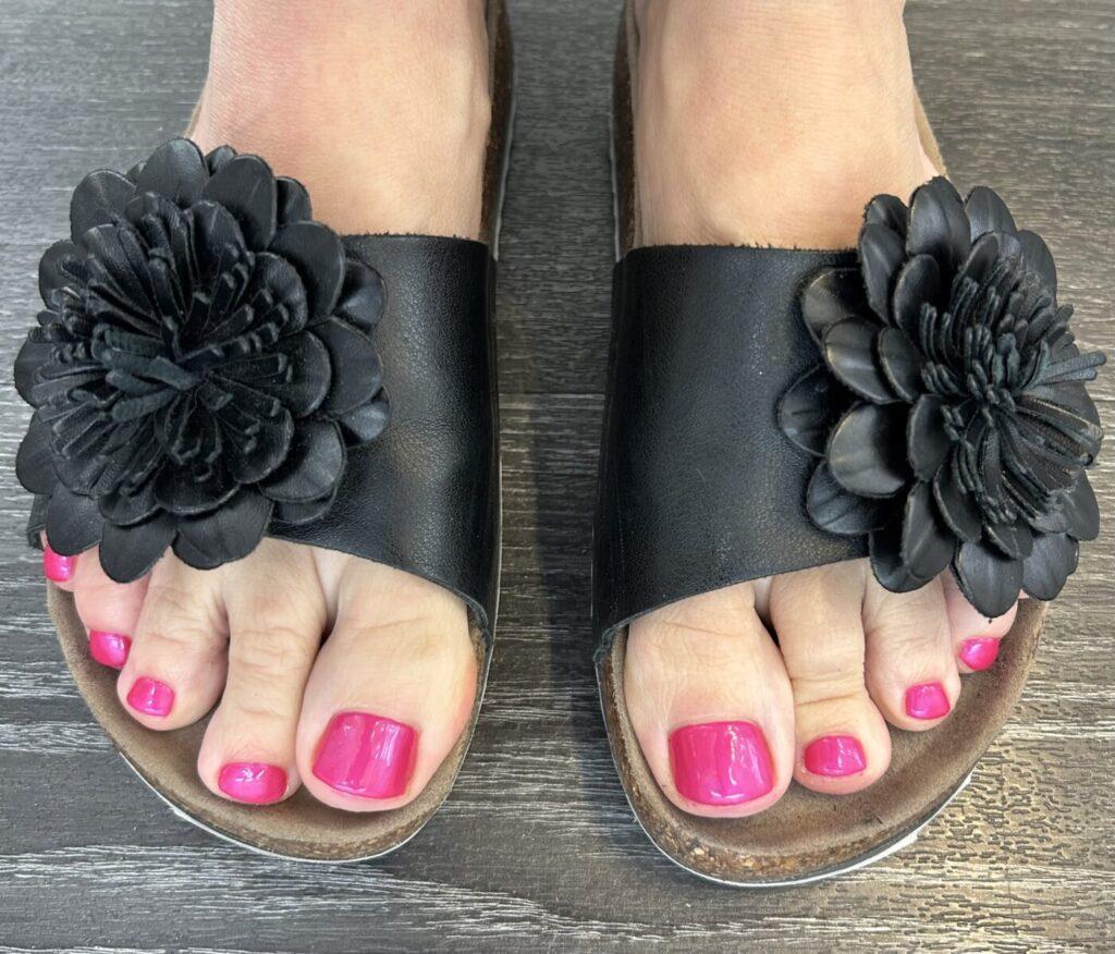 Schwarze Sandalen mit Blumenapplikation und pink lackierten Fußnägeln
