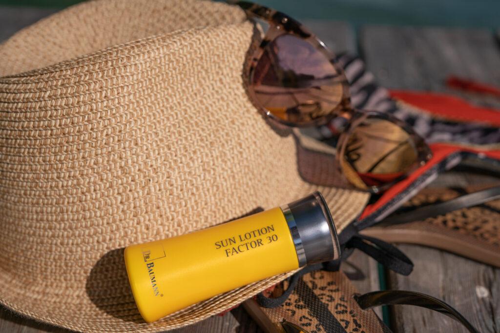 Sonnencreme mit Faktor 30 auf einem Strohhut und Sonnenbrillen